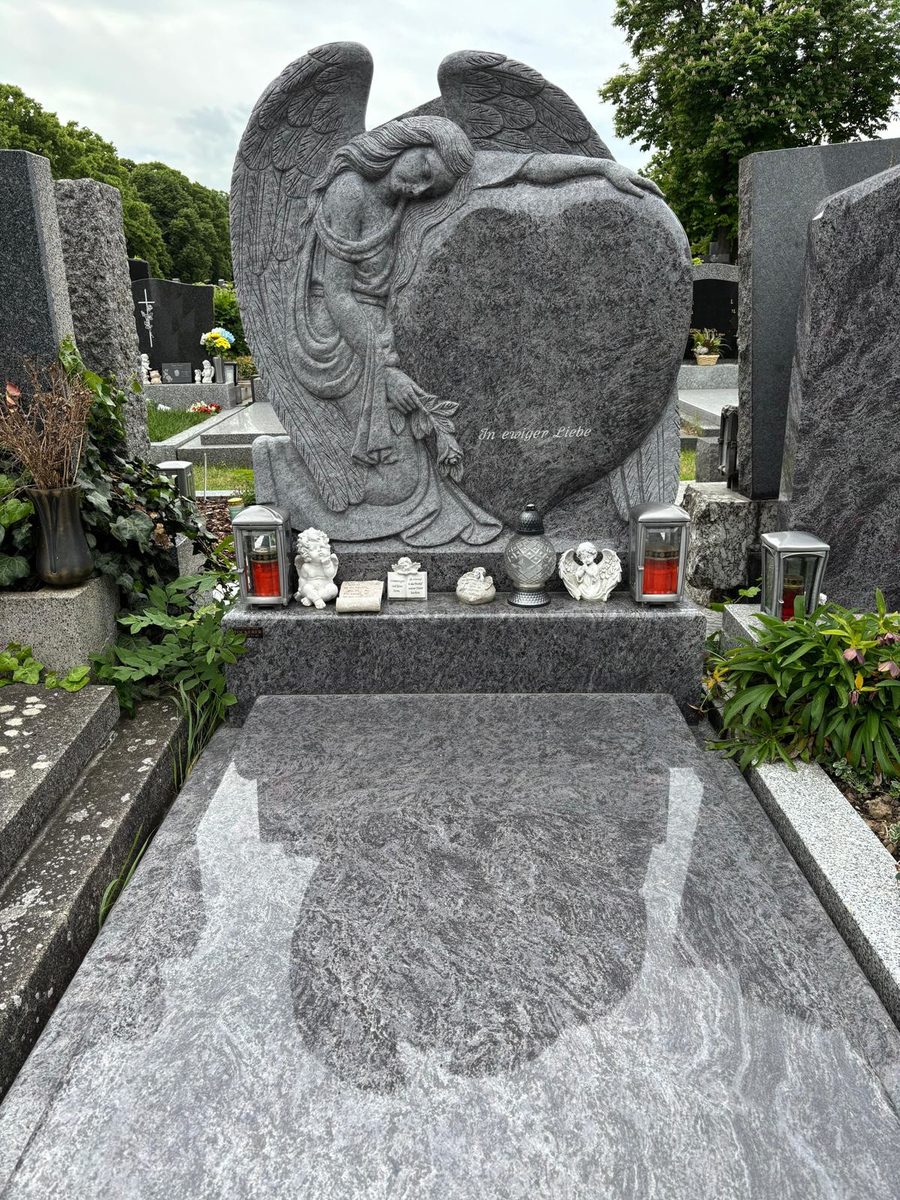Grabanlage aus Orion-Granit mit gemeißeltem Engel, der sich an ein Herz lehnt, Inschrift In ewiger Liebe, polierter Deckplatte und Laternen aus Aluminium am Atzgersdorfer Friedhof