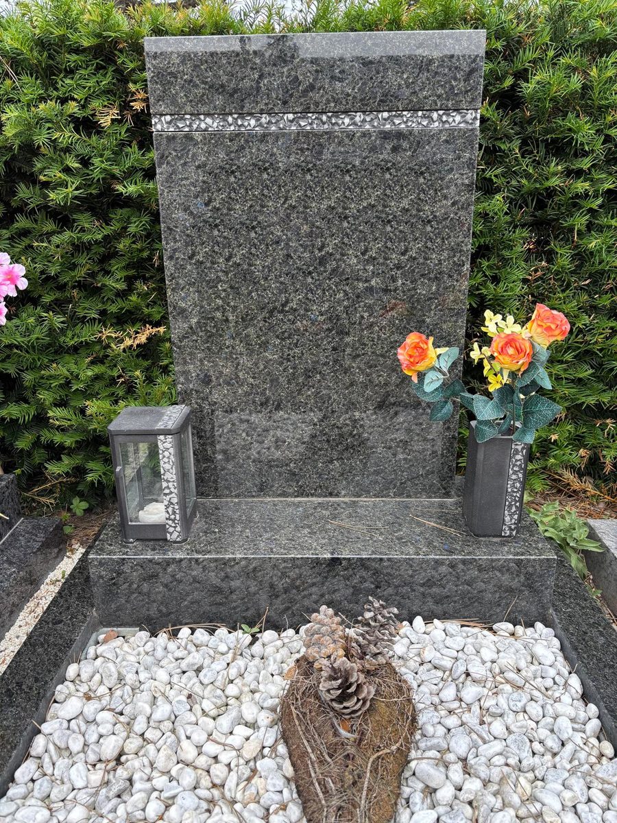 Grabstein aus dunklem Steel-Grey-Granit mit Zierband, passender Laterne und Vase sowie Grabfläche mit weißem Zierkies am Baumgartner Friedhof