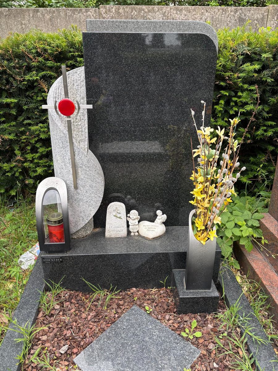 Grabstein aus dunklem Impala-Granit mit hellem Granitelement, Aluminiumkreuz mit roter Glaseinlage sowie Laterne und Vase aus Aluminium am Meidlinger Friedhof