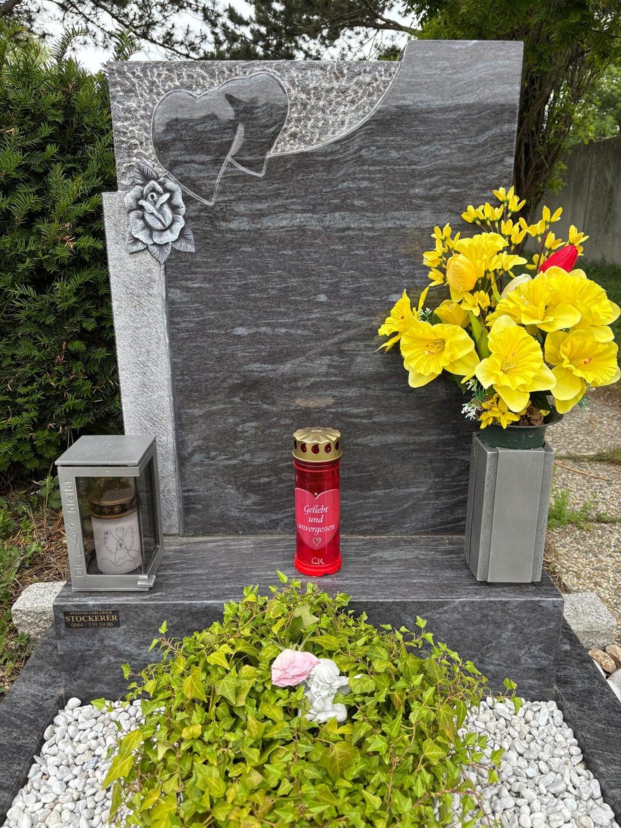 Grabstein aus Silk-Blue-Granit mit zwei Herzen auf gestocktem Grund und gemeißelter Rose sowie Laterne und Vase aus Aluminium am Friedhof Mödling