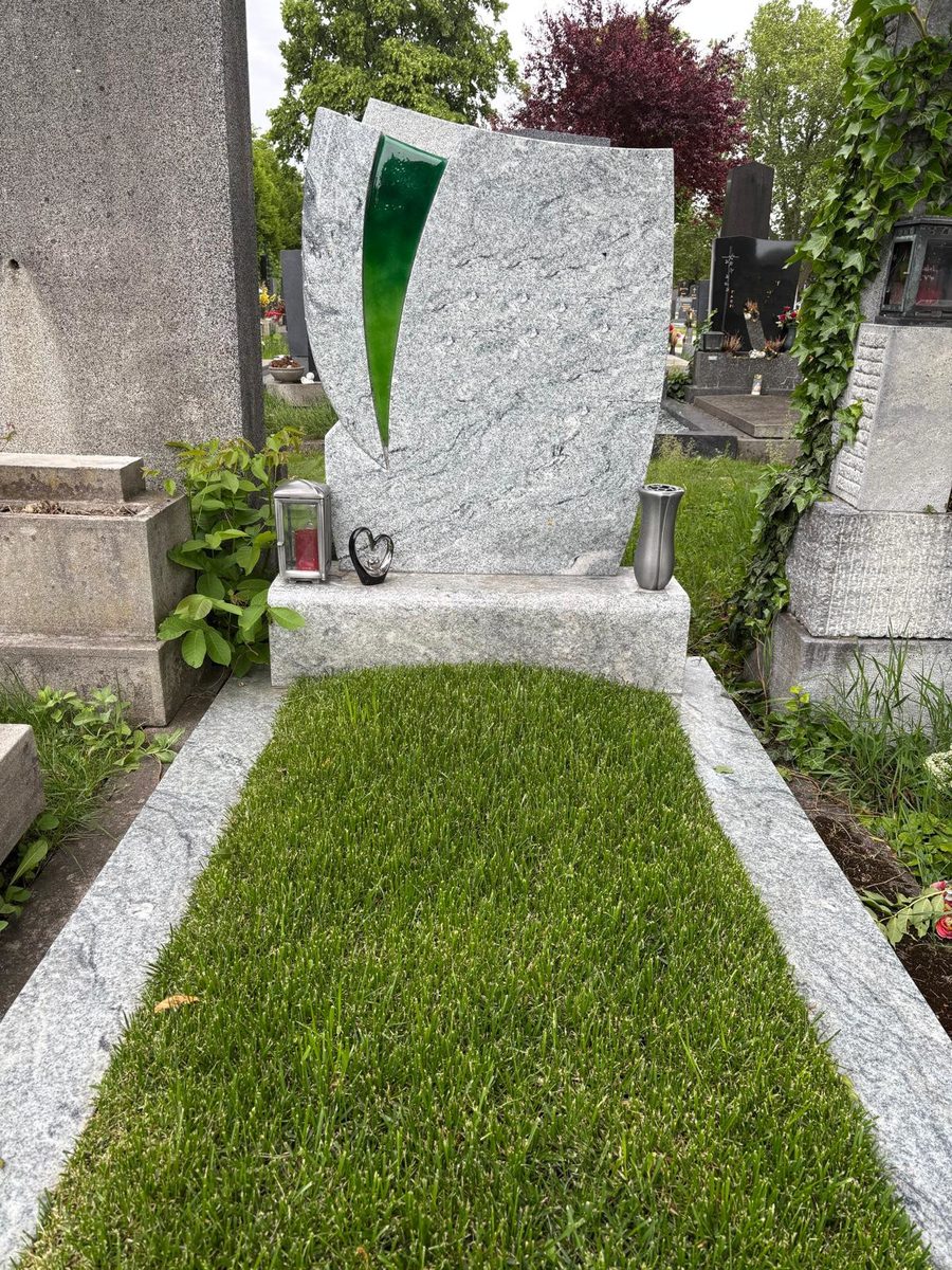Moderner Grabstein aus hellem Viscont-White-Granit mit grüner Glaseinlage, Einfassung aus Granit sowie Laterne und Vase aus Aluminium am Friedhof Oberlaa