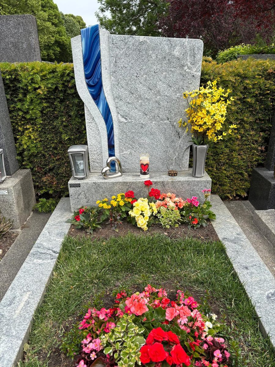 Grabstein aus hellem Viscont-White-Granit mit geschwungener blauer Glaseinlage, Einfassung aus Granit sowie Laterne und Vase aus Aluminium am Friedhof Perchtoldsdorf