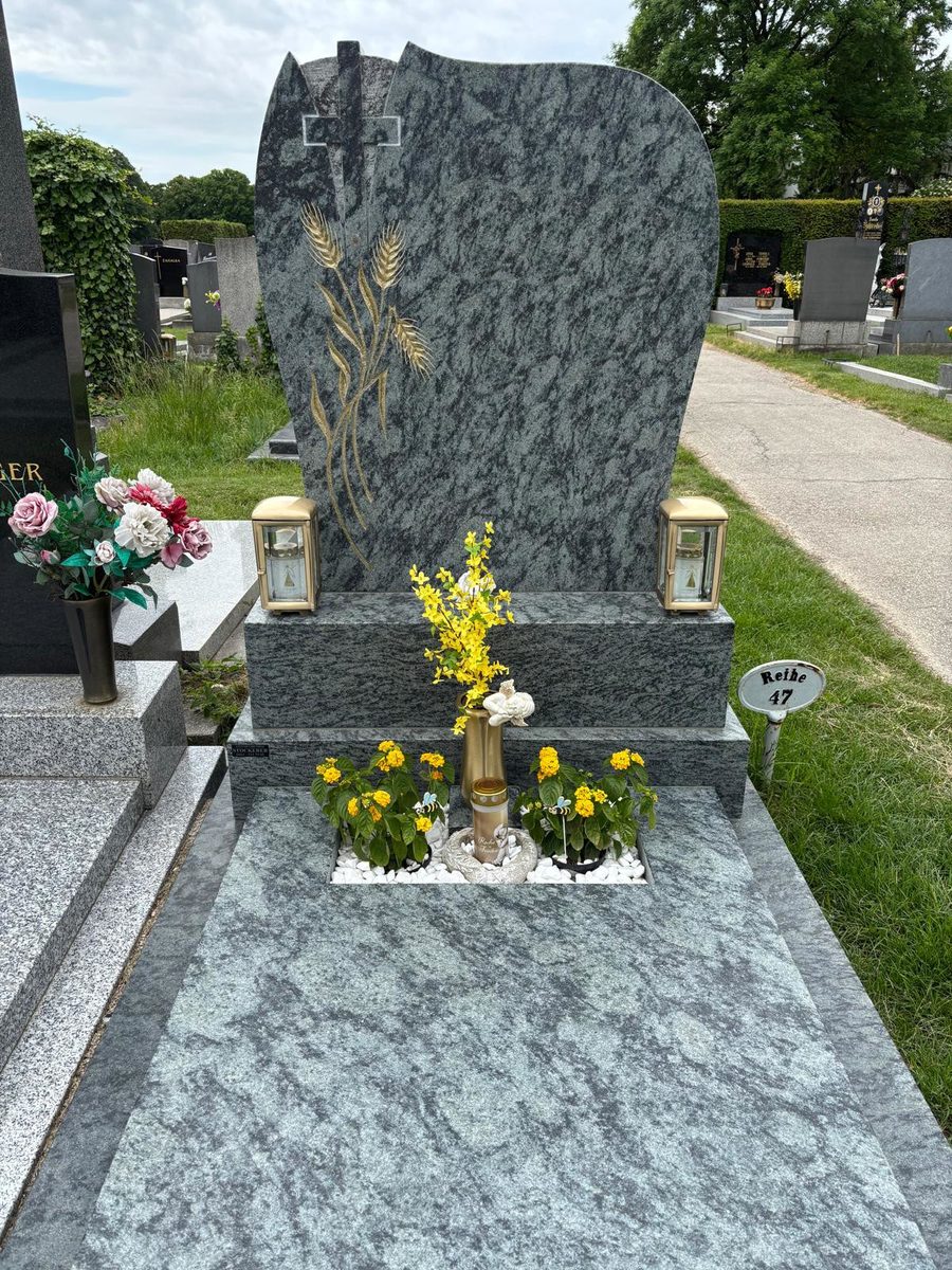 Grabanlage aus grünem Olive-Green-Granit mit Kreuz und goldenen Ähren, Pflanzfläche in der Deckplatte sowie Laternen und Vase aus Bronze am Pfarrfriedhof Schwechat