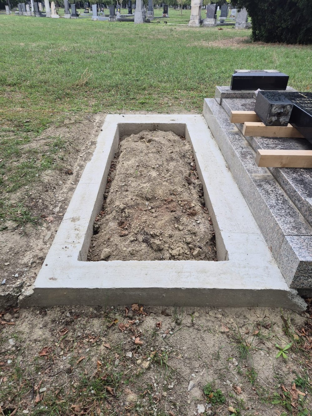 Frisch gesetztes, sauberes Betonfundament für eine Grabanlage neben einem bestehenden Grabstein