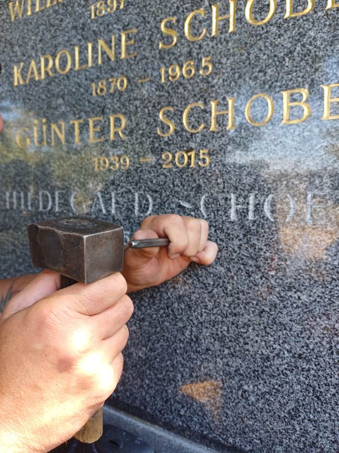 Steinmetz graviert eine Inschrift von Hand mit Hammer und Meißel am Zentralfriedhof